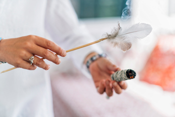 person holding a feather and a smudge stick with smoke rising in a serene setting featuring 11 elements of tranquility and cleansing