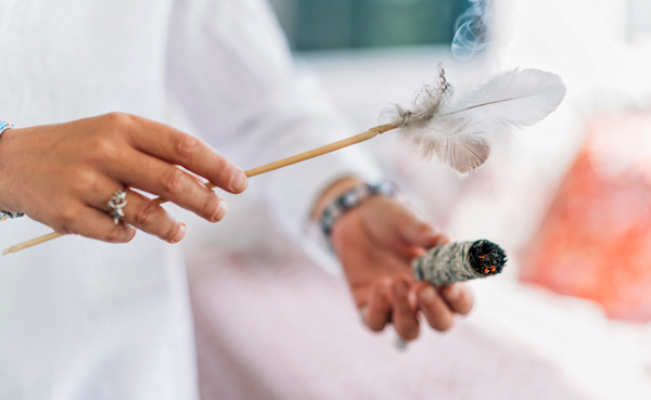 person holding a smudge stick with smoke and a feather performing cleansing ritual for spiritual energy 2 important elements 2 purification techniques