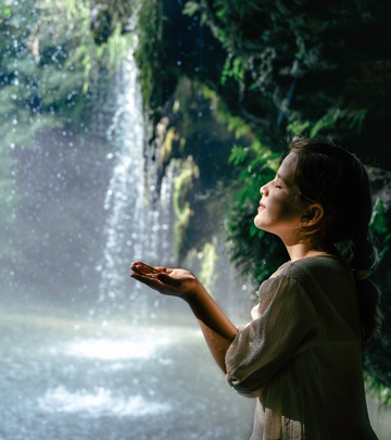 young girl standing near waterfall enjoying nature's beauty in a serene moment receiving water droplets 4 natural wonders