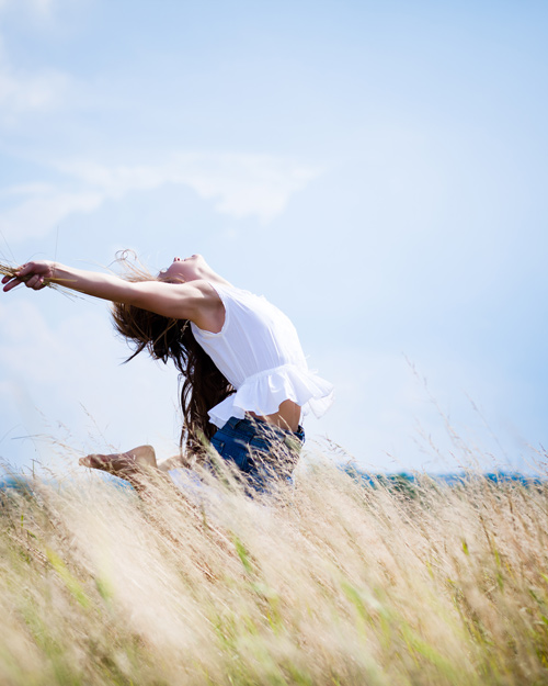 woman jumping joyfully in a field under a blue sky representing freedom and vitality with seven shades of nature surrounding her