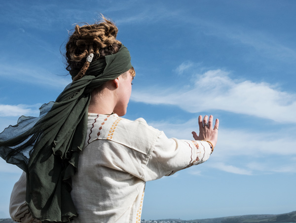 person with curly hair wearing a headscarf and traditional clothing reaching out towards the sky in a scenic outdoor setting representing cultural expression and connection to nature 2 different views