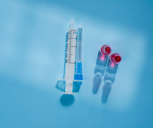 syringe and vials on blue surface medical supplies for vaccine research and injections