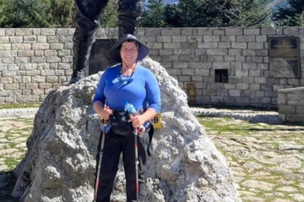 woman standing on rock with hiking poles in front of statue during outdoor adventure exploring 6 summits